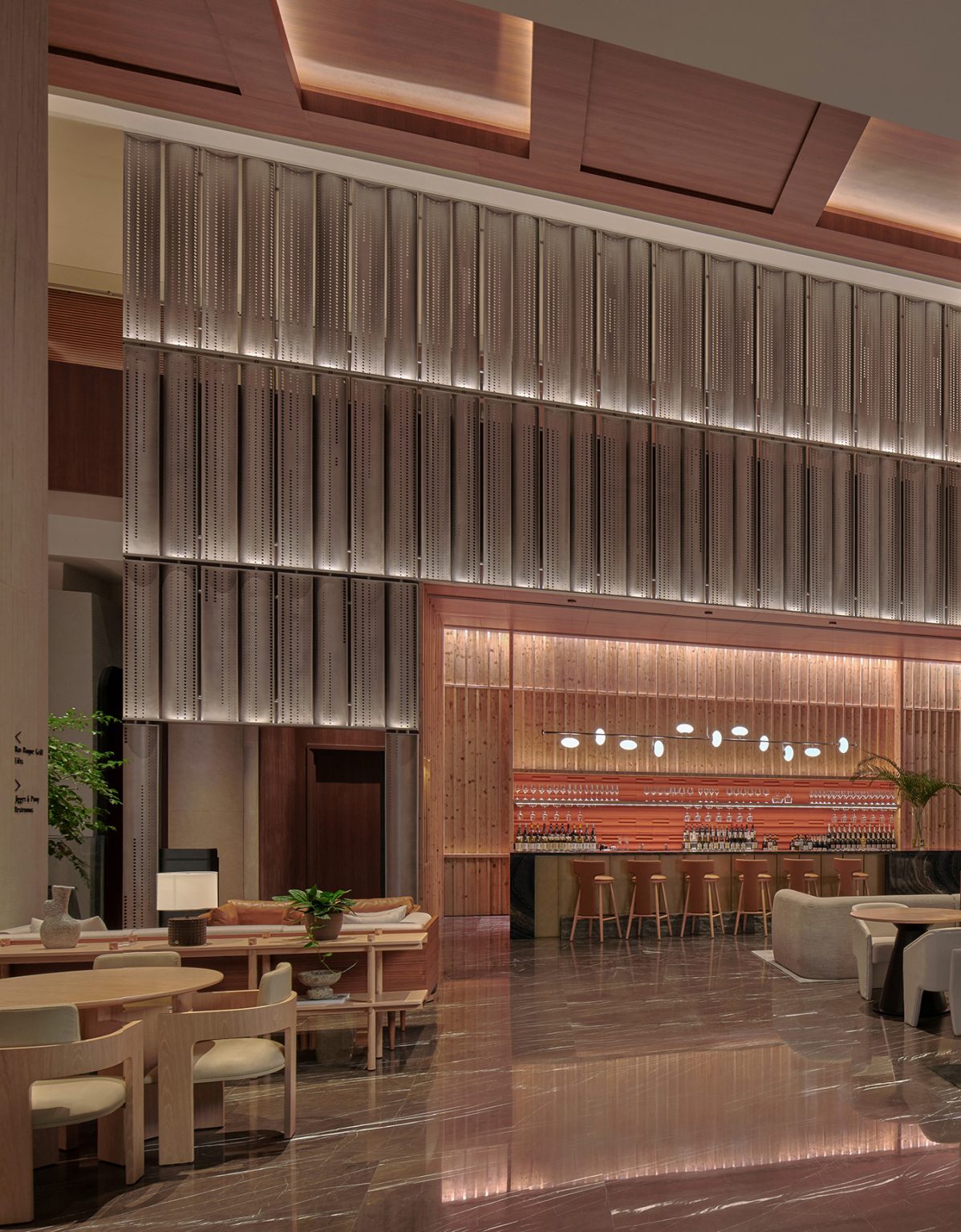 Modern hotel lobby with high ceilings, featuring a central tall tree, elegant seating, a stylish bar with hanging lights, and a serene ambience.