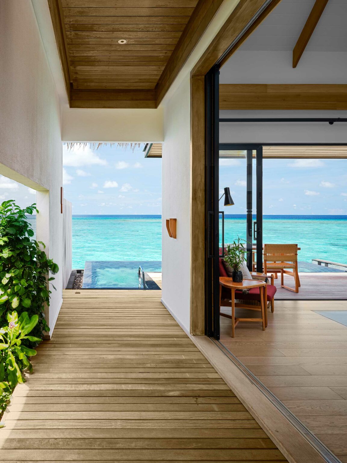 Ocean view from a luxurious, open-plan room with wooden floors. A tranquil pool leads to turquoise sea and sky, evoking relaxation and serenity.