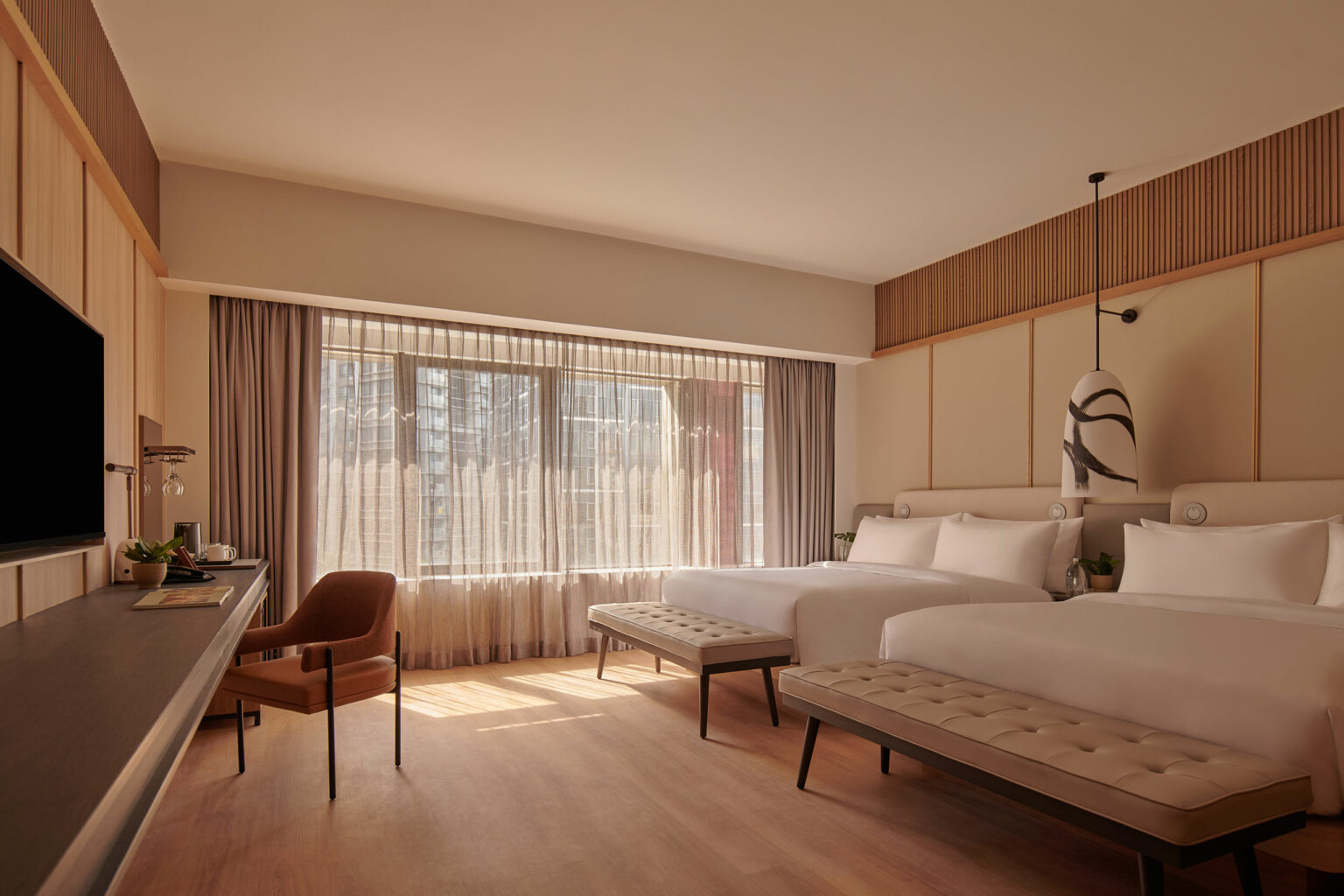 Modern hotel room with two plush double beds, a wooden accent wall, large window with sheer curtains, and elegant lighting, creating a serene ambiance