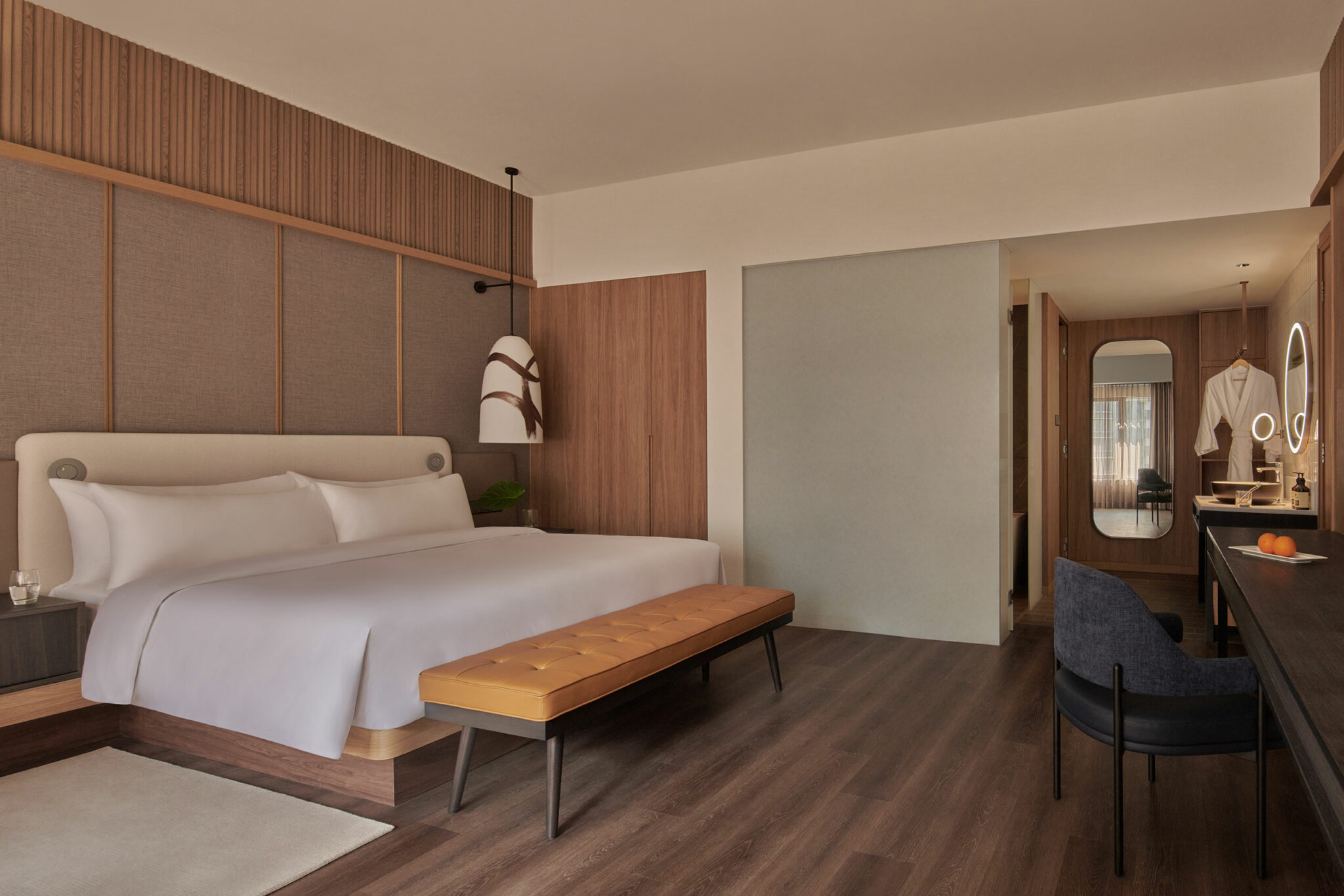 Modern hotel room with a large bed, wooden accents, and a sleek design. Features a bench at the foot of the bed and a stylish vanity area. Warm and inviting.