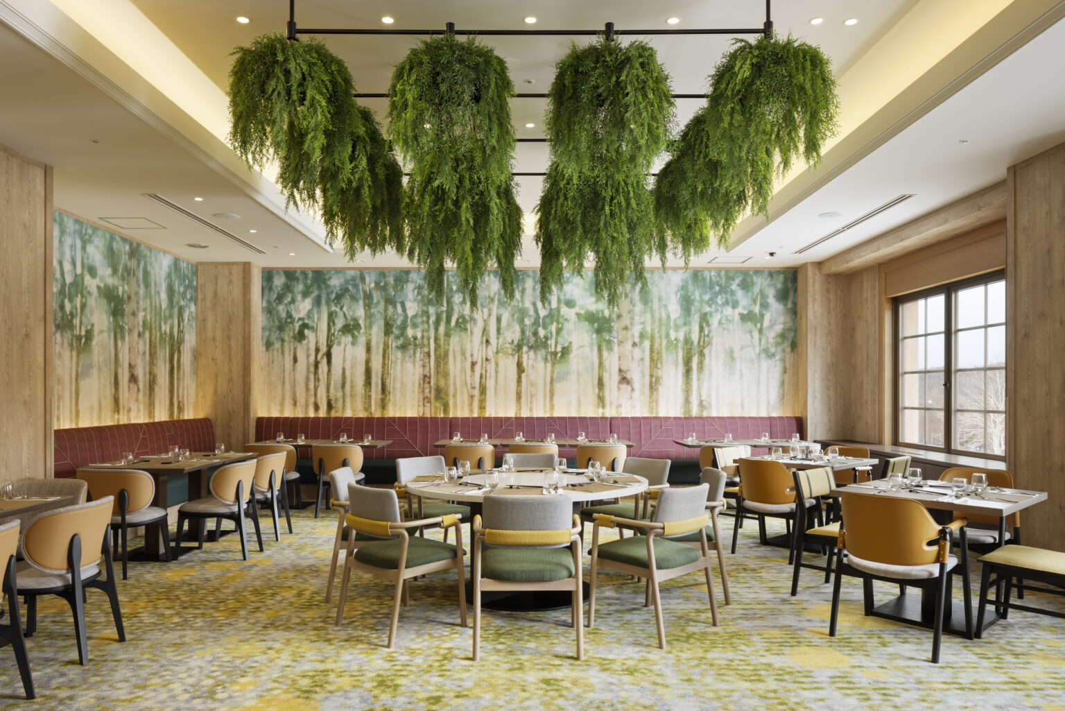 Elegant restaurant interior with hanging greenery, round and rectangular tables set for dining. Forest-themed wall art creates a serene, natural ambiance.