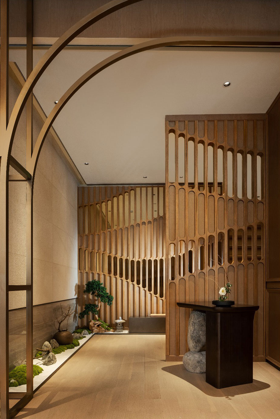 Warm, minimalist interior with a wooden lattice partition, an elegant bonsai on the left, and a dark table with a potted plant on the right.