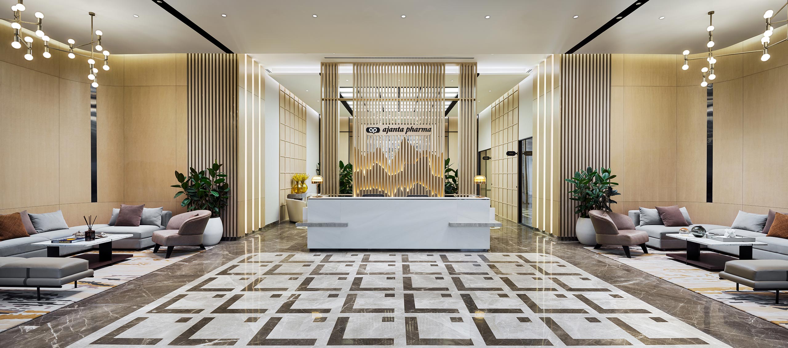 Spacious modern lobby with a geometric patterned floor, central sleek white reception desk, sofas and chairs, warm lighting, and decorative plants.