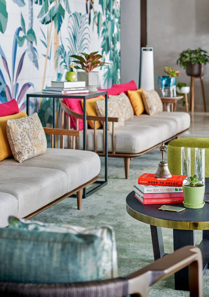Stylish two beige sofas adorned with colorful cushions, tropical wall art, and books on tables. Vibrant, cozy, and modern setting.