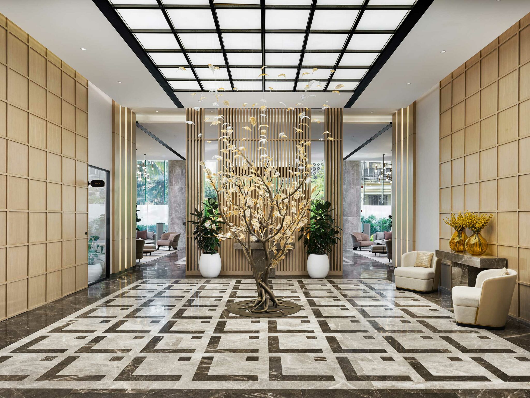 Luxurious lobby with a geometric-patterned marble floor and a striking central sculpture resembling a tree. Elegant seating and plants create a refined ambiance.