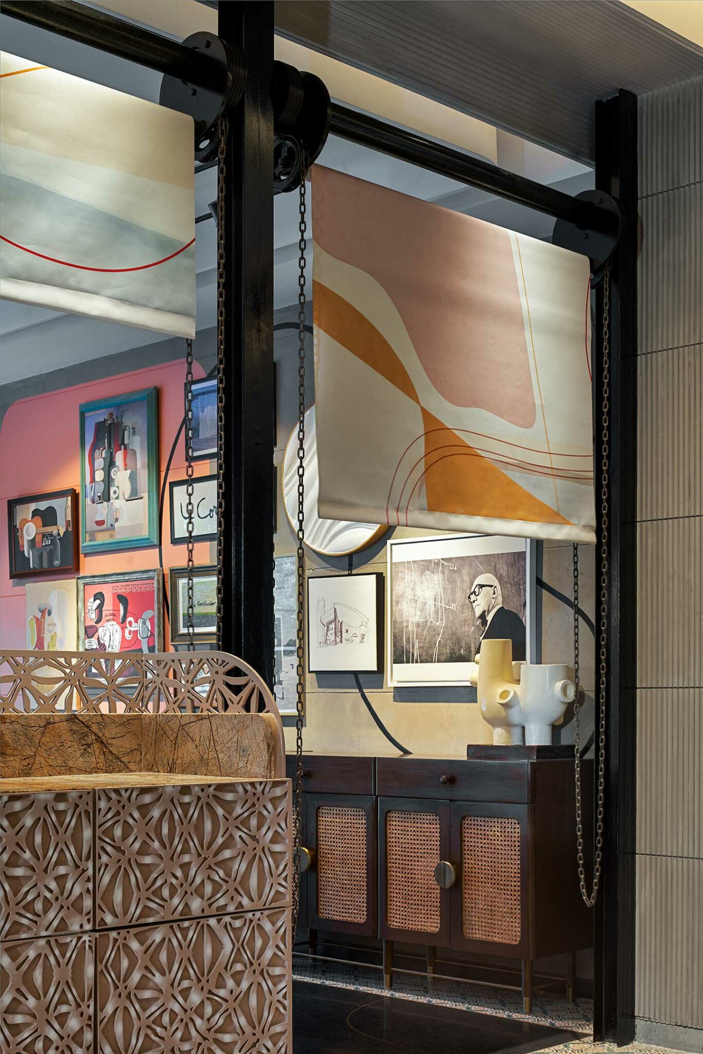 Interior view of a gallery with abstract art on walls and textiles. A wood cabinet with circular patterns sits in the foreground, conveying a modern, artistic ambiance.