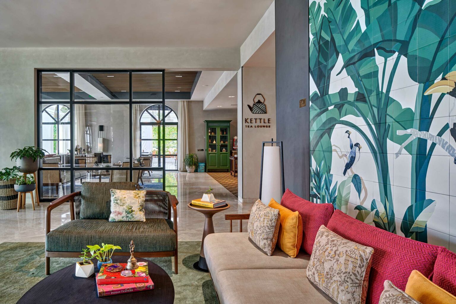 A modern lounge with tropical decor, featuring a colorful mural of leaves and birds. Cozy sofas with vibrant pillows create a relaxing atmosphere.