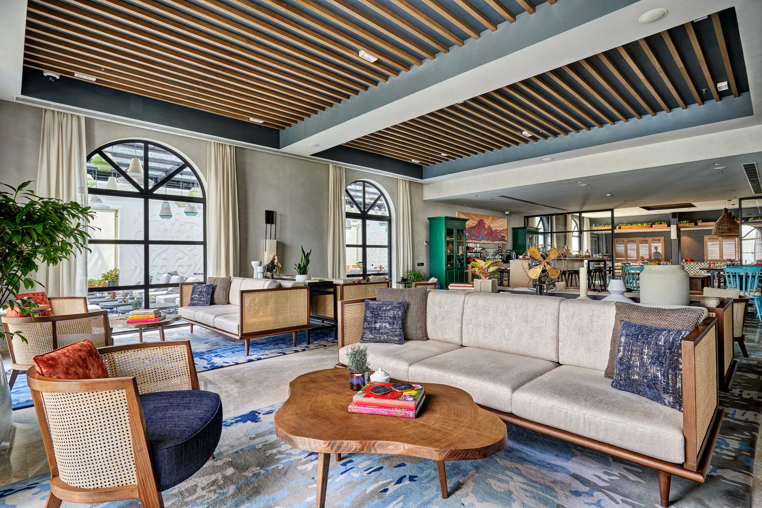 Modern lounge with open design, featuring beige sofas, a wooden coffee table, blue accents, large arched windows, and a cozy, inviting ambiance.