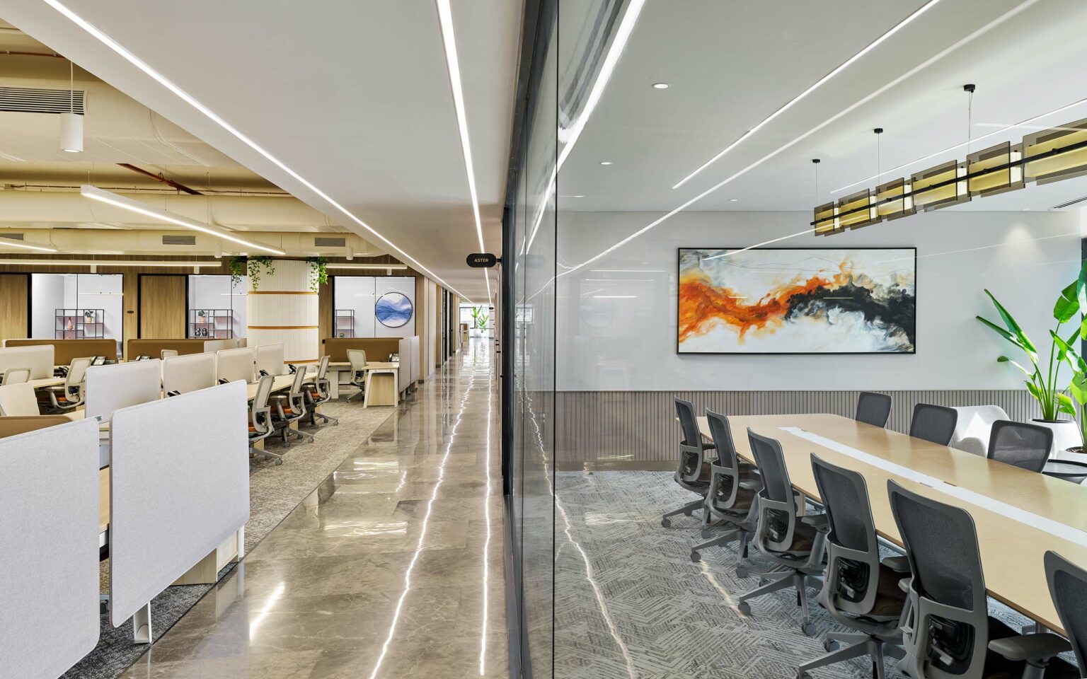 Modern open office with a sleek design. Left side has workstations and hanging plants; right side features a conference room with abstract art and a large table, conveying a professional and stylish atmosphere.
