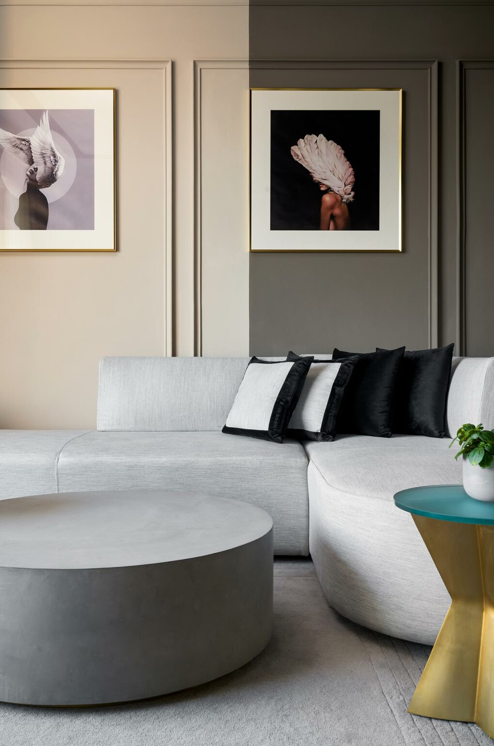 A modern living room with a light gray curved sofa, black and white cushions, round gray coffee table, teal side table, and framed art on gray walls.