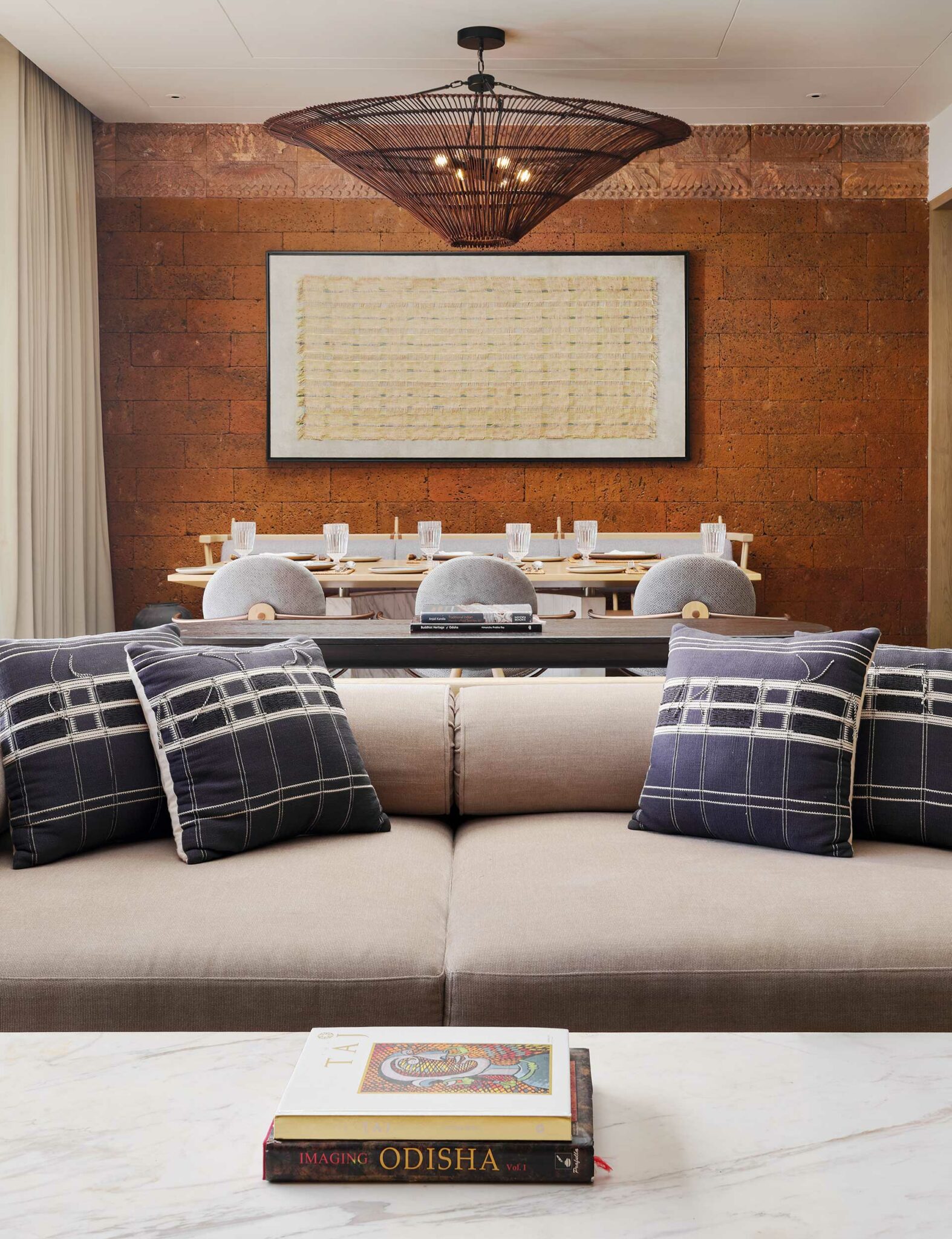 Sophisticated living area with beige sofa, blue plaid pillows, and a marble table featuring books. Distinctive pendant light and art adorn the warm-toned wall.