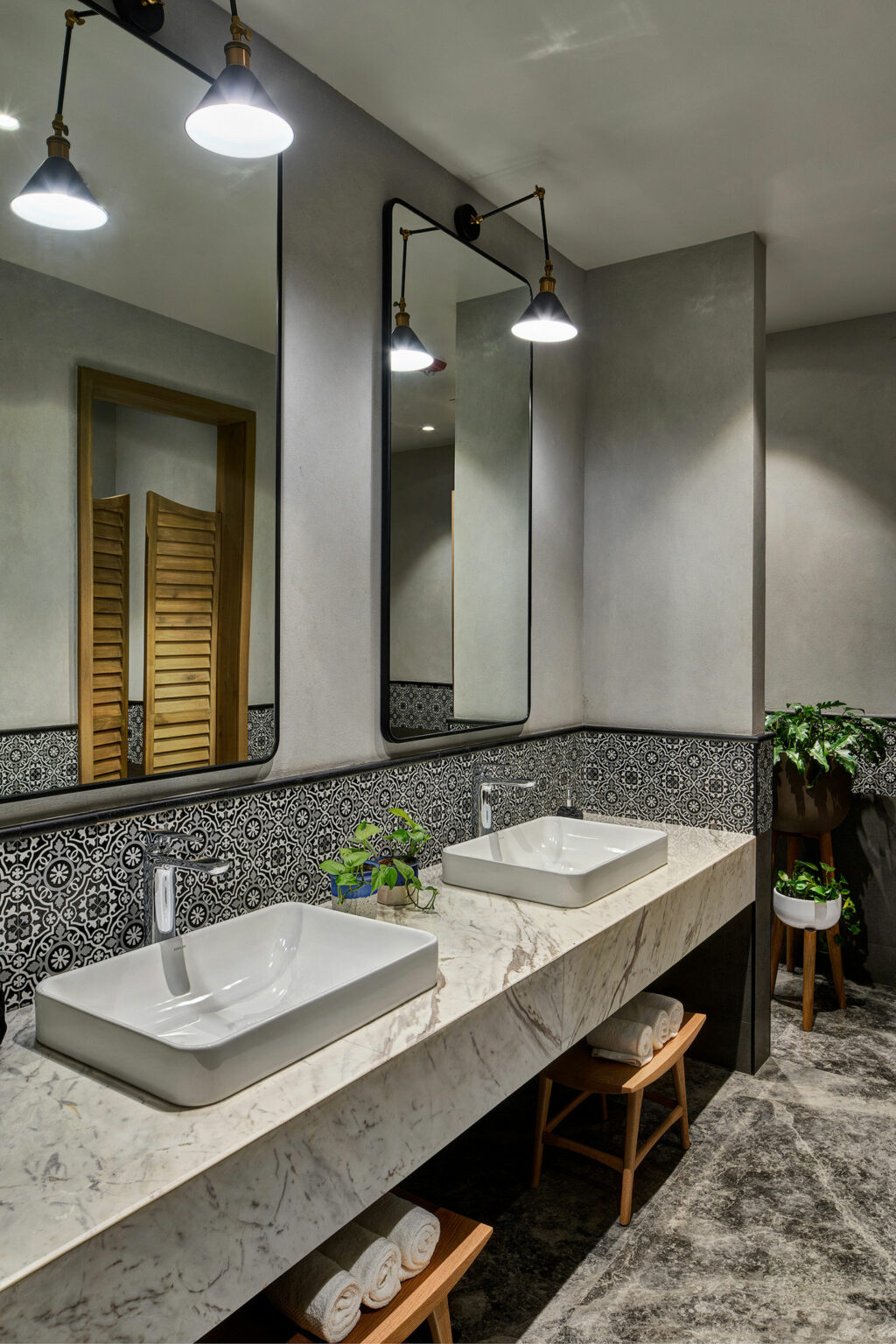 Modern bathroom with two rectangular sinks on a marble countertop, under large mirrors. Decorative tiles, plants, and warm lighting add elegance.