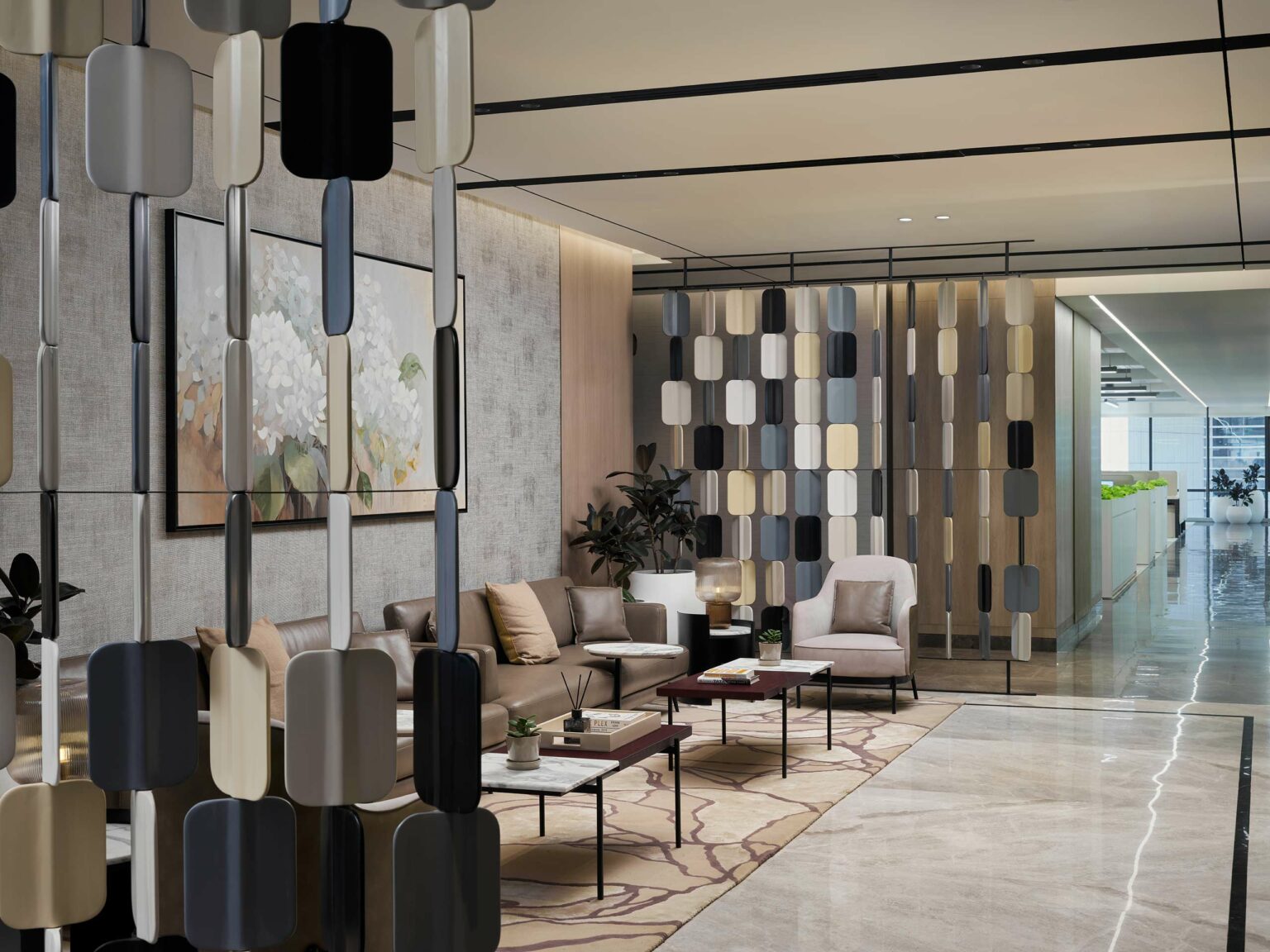 Modern office lounge with neutral tones, featuring beige sofas, stylish partitions, a patterned rug, and indoor plants. The atmosphere is calm and inviting.