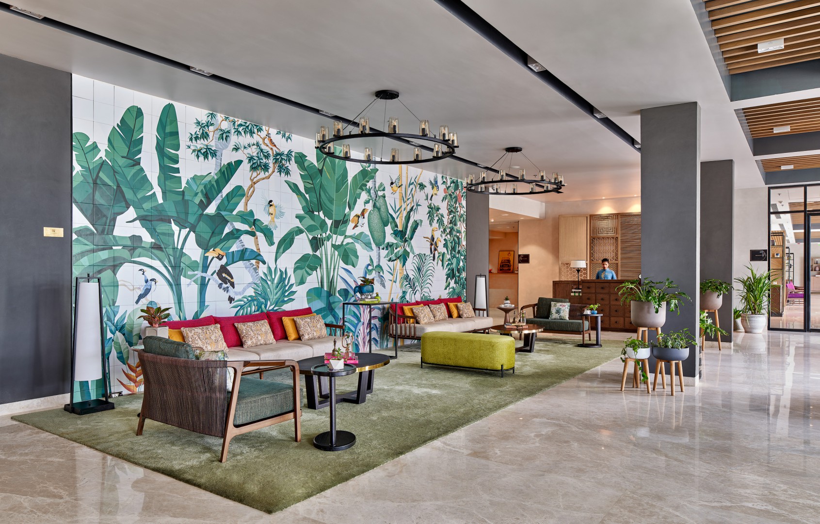 Modern hotel lobby with vibrant tropical mural of large green leaves. Features plush seating with colorful cushions, sleek lighting, and a welcoming atmosphere.