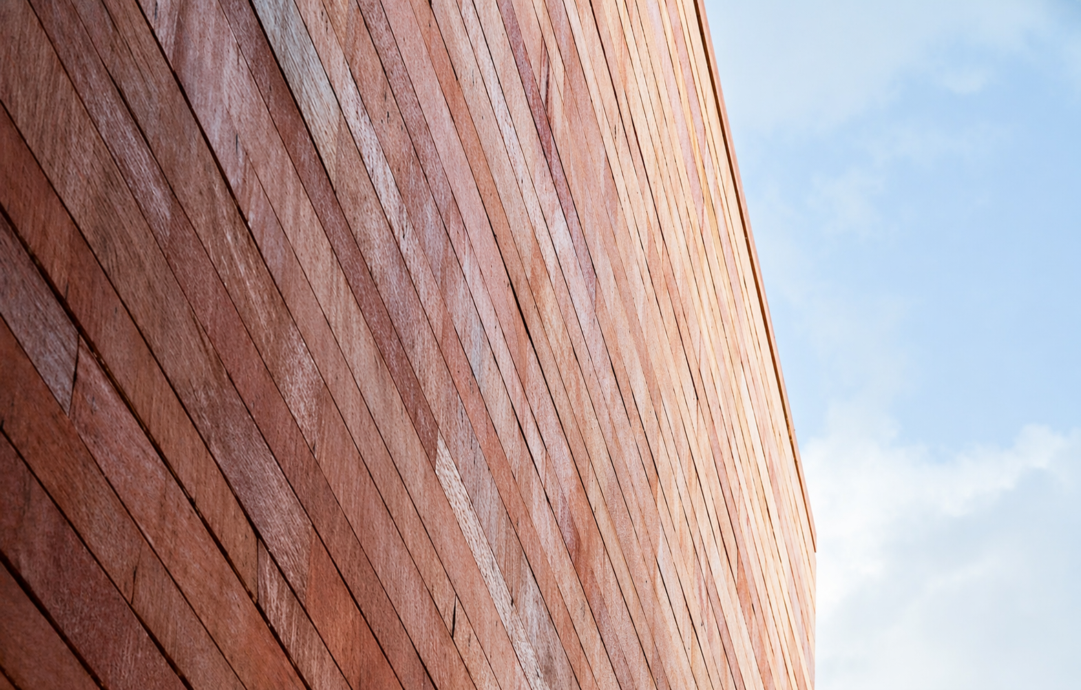 Red Sandstone facade with horizontal panels forms a towering wall against a soft blue sky. The image conveys a sense of height and modern architecture.
