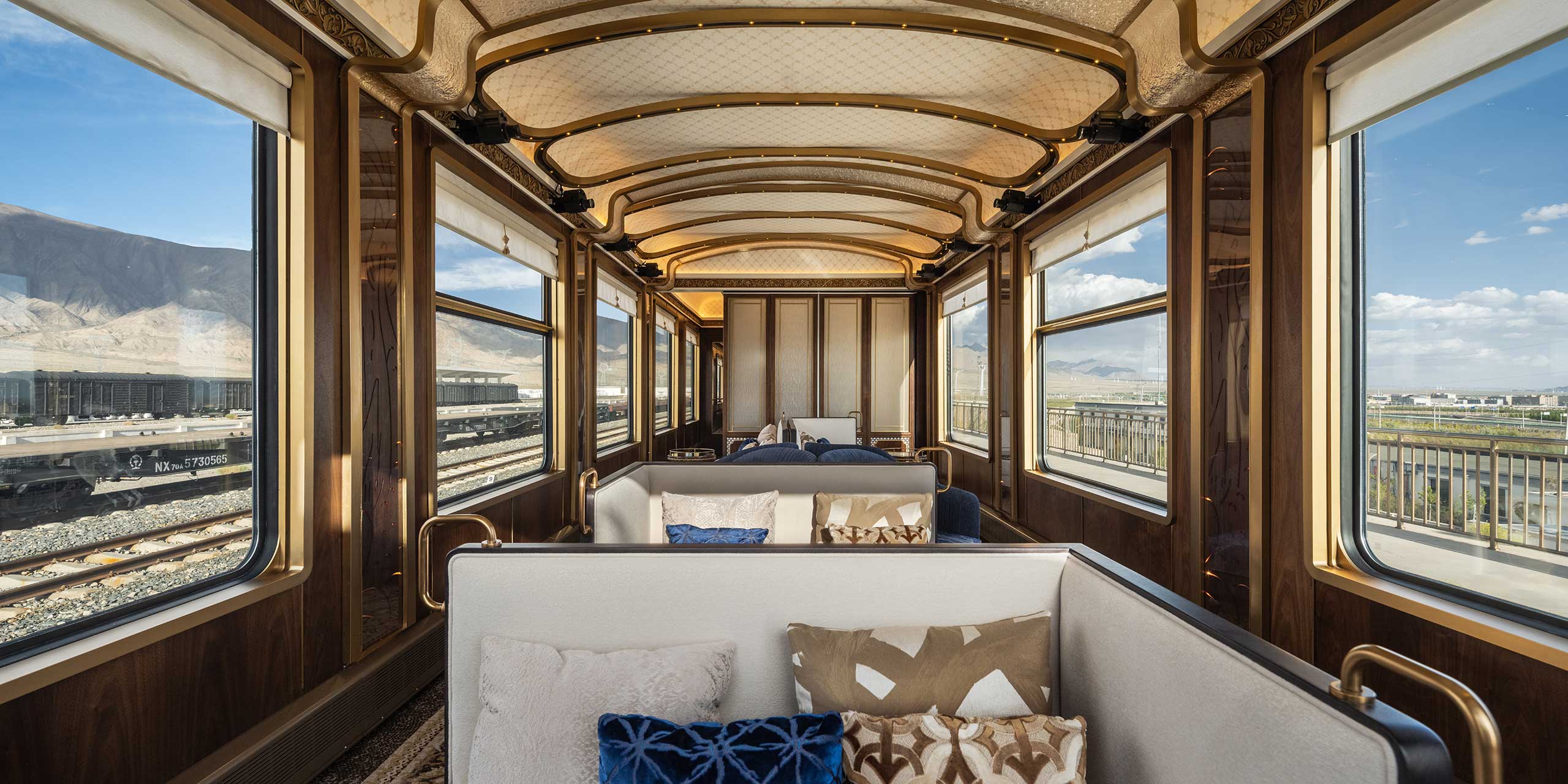 A luxurious train cabin with panoramic windows shows scenic mountain views. Elegant wood paneling and plush pillows create a sophisticated, tranquil ambiance.