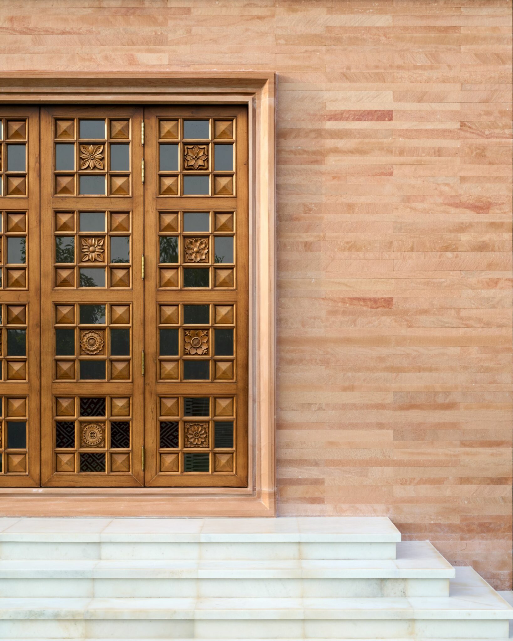 Ornate wooden door with intricate patterns, set in a light brown stone wall. The door sits atop white marble steps, conveying a sense of elegance.