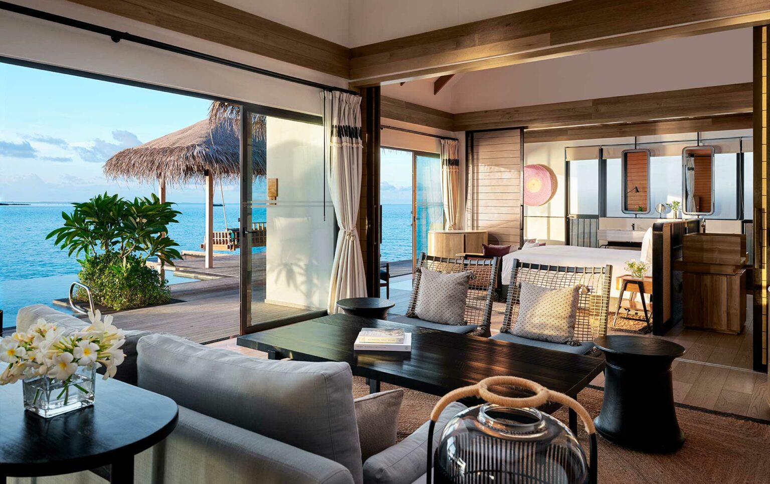 Luxurious overwater villa interior with ocean view, featuring a cozy seating area, large windows, wooden decor, and serene, tropical ambiance.