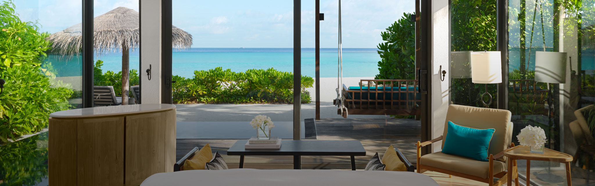 Luxurious beachfront room with a view of turquoise ocean and white sand. Cozy seating, turquoise cushions, and modern decor create a serene, inviting atmosphere.