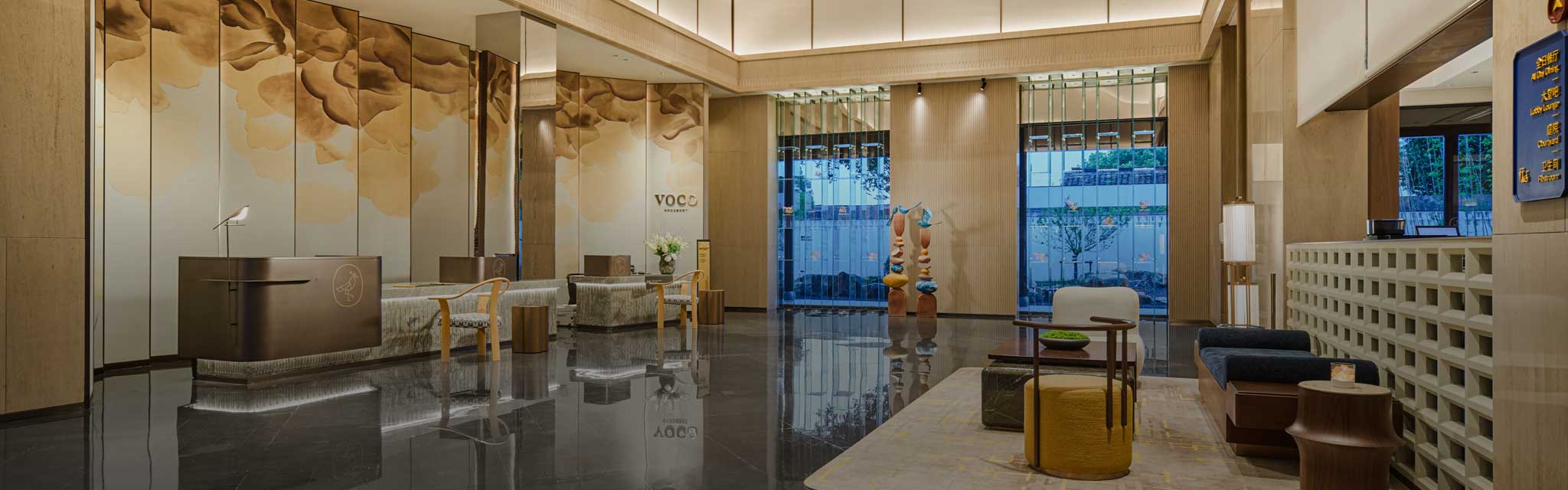 A modern hotel lobby with a sleek design, featuring a brown reception desk, large floral wall art, soft lighting, and stylish seating, conveying elegance.