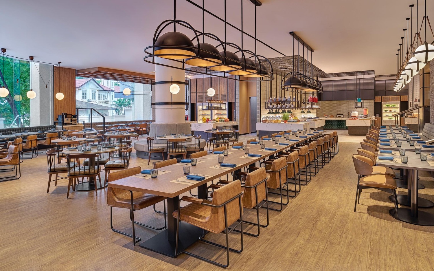 Spacious, modern restaurant with wooden floors, long tables set with blue napkins, stylish pendant lights, and large windows. Warm and inviting atmosphere.