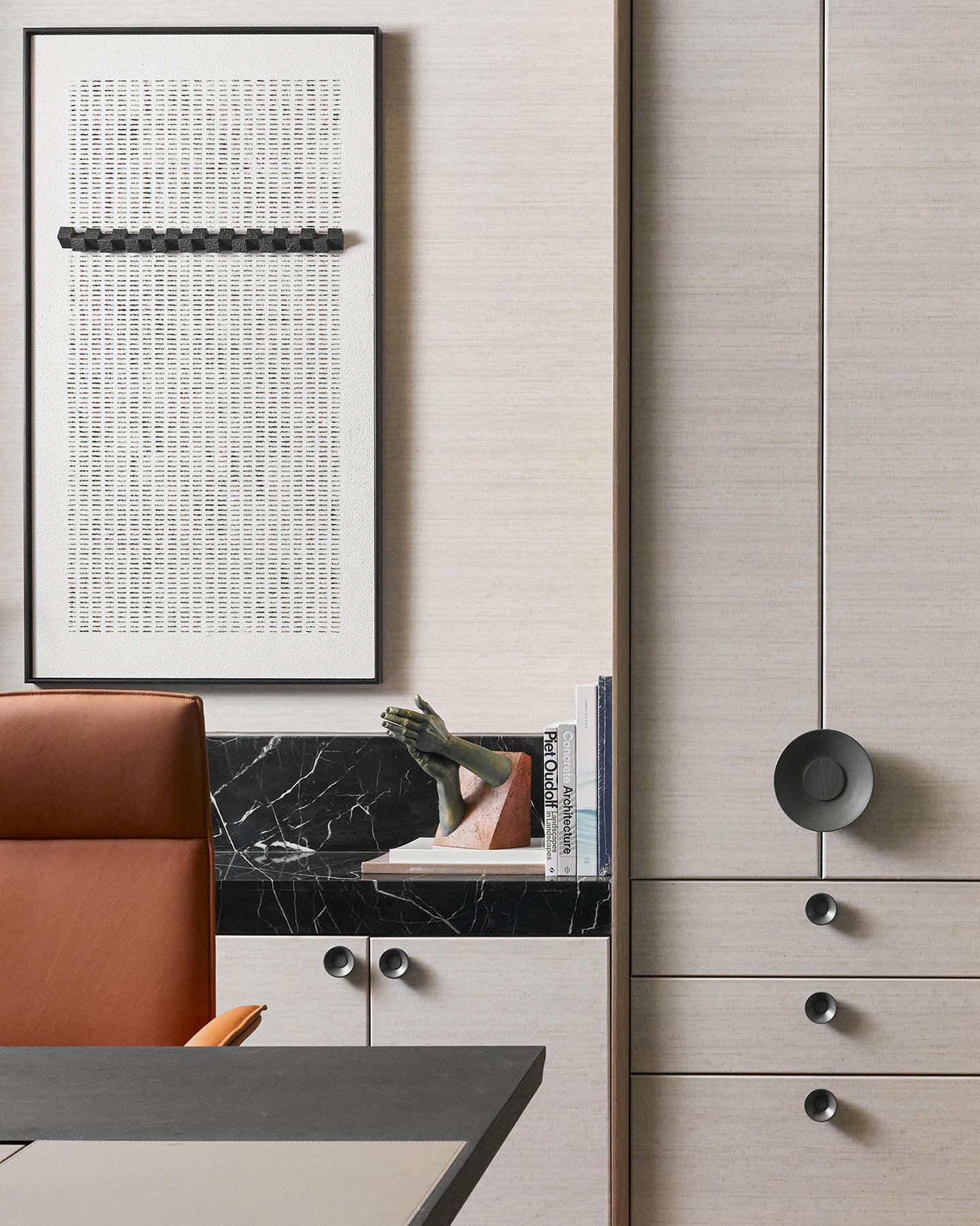 Modern office interior with a brown leather chair, black marble desk, and abstract wall art. Sculpture and books sit on a sleek black cabinet.