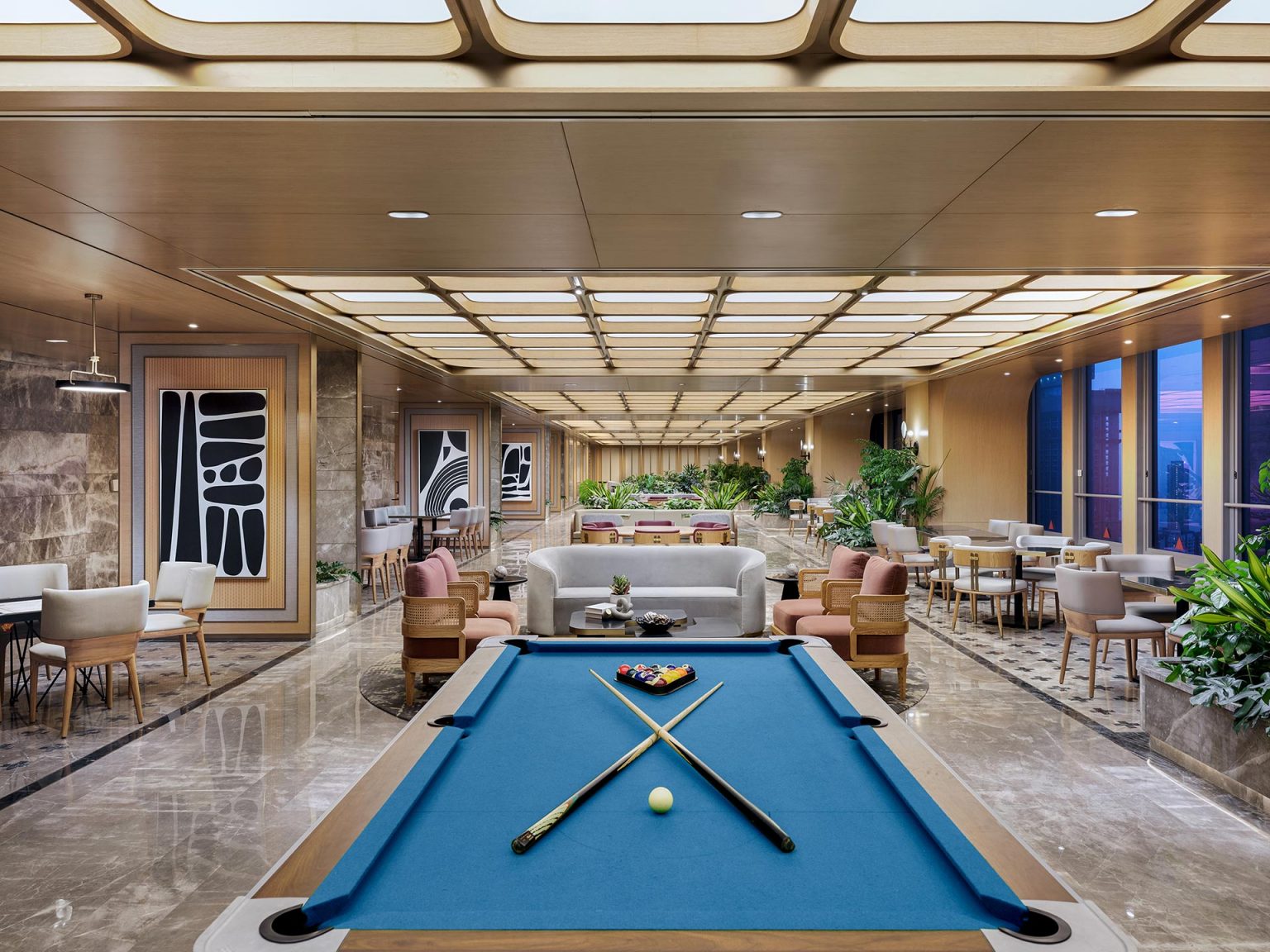 Luxurious lounge with a blue billiard table in the foreground. Modern seating, warm lighting, and large windows creating an elegant ambiance.