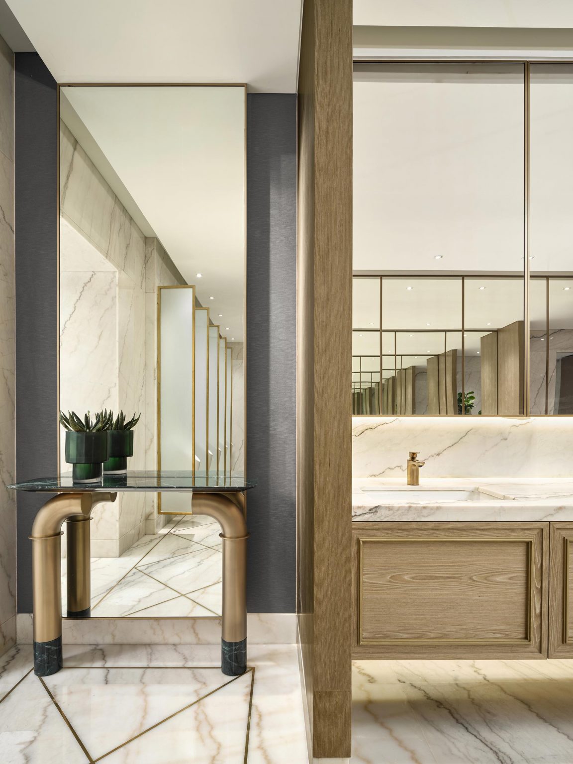 Modern bathroom with a marble sink and mirrored wall reflecting sleek surfaces. A decorative glass table holds potted plants, enhancing elegance.