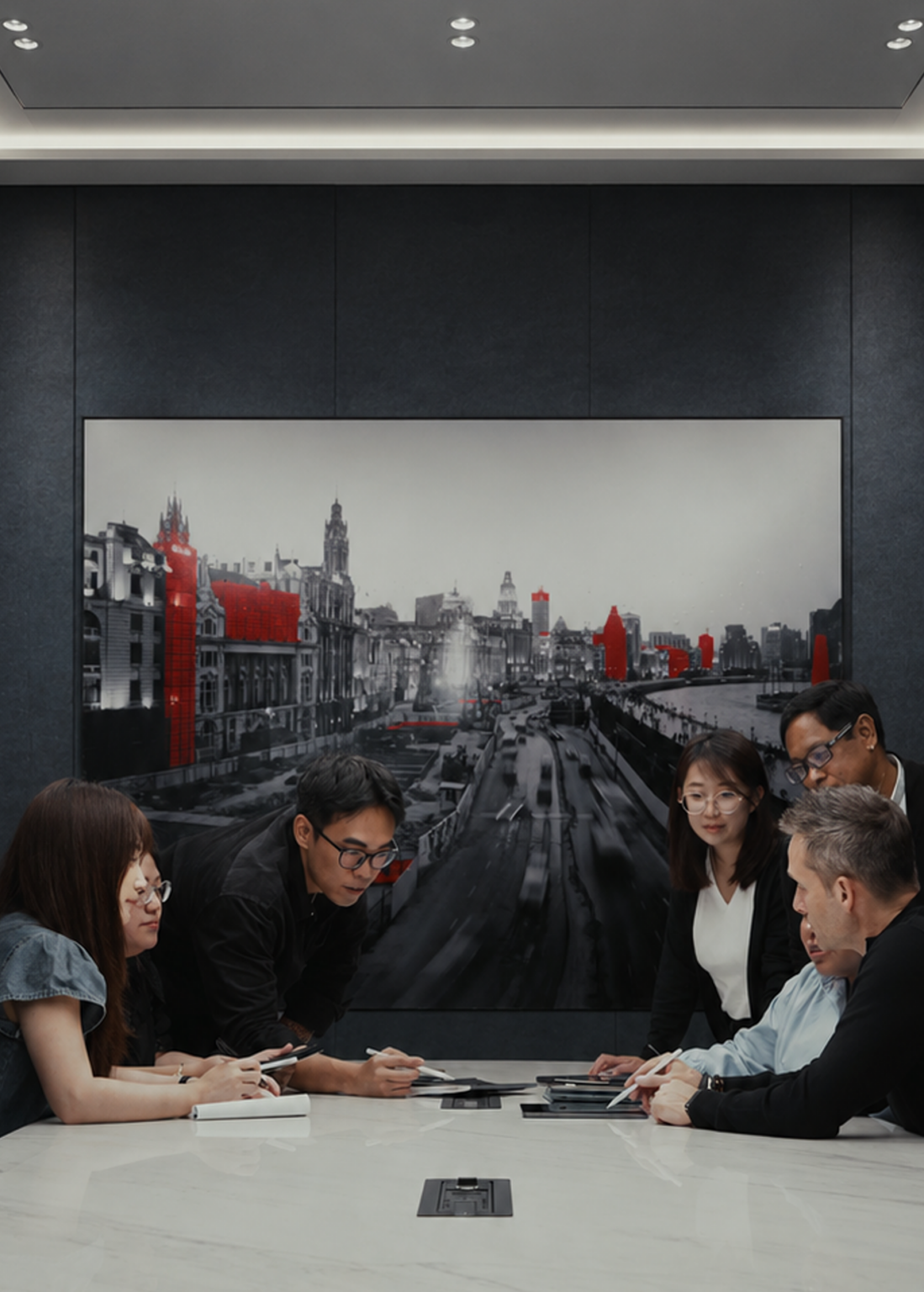 A group of six people collaborates at a conference table, with a black-and-white cityscape photo behind them featuring buildings highlighted in red.