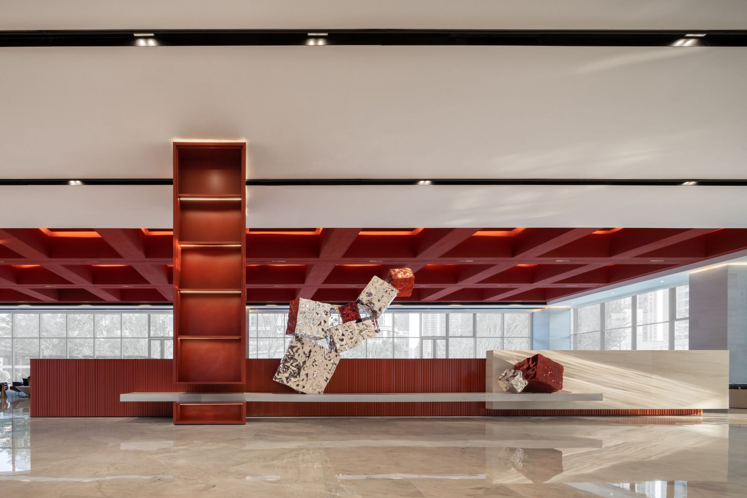 Modern interior with a striking red ceiling and abstract geometric sculptures. Large windows allow natural light, enhancing the open, contemporary feel.