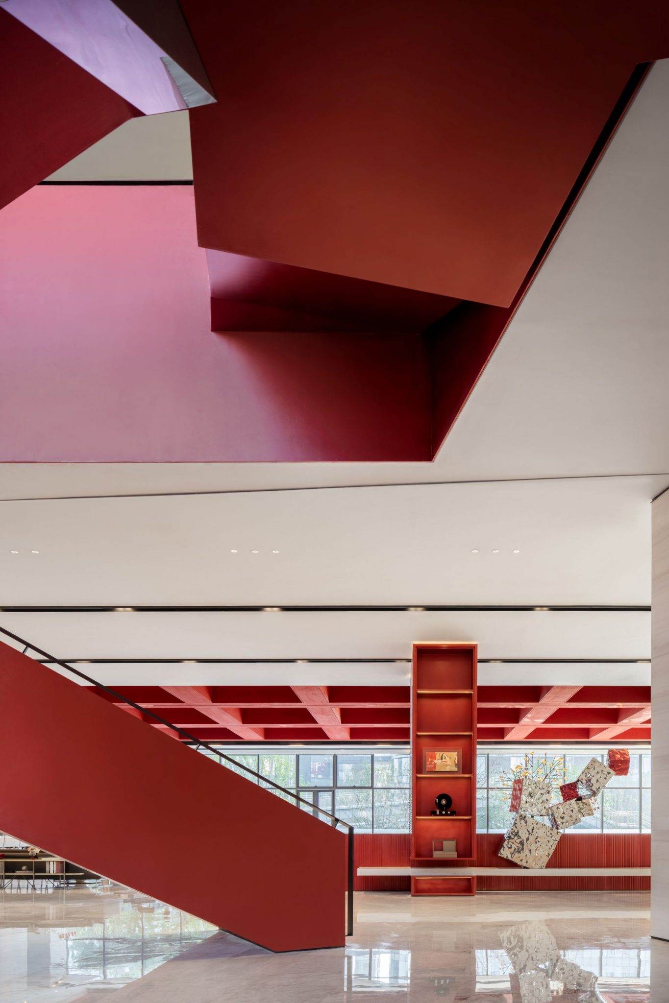 A modern interior space featuring geometric red design elements and a staircase, with large windows letting in natural light.