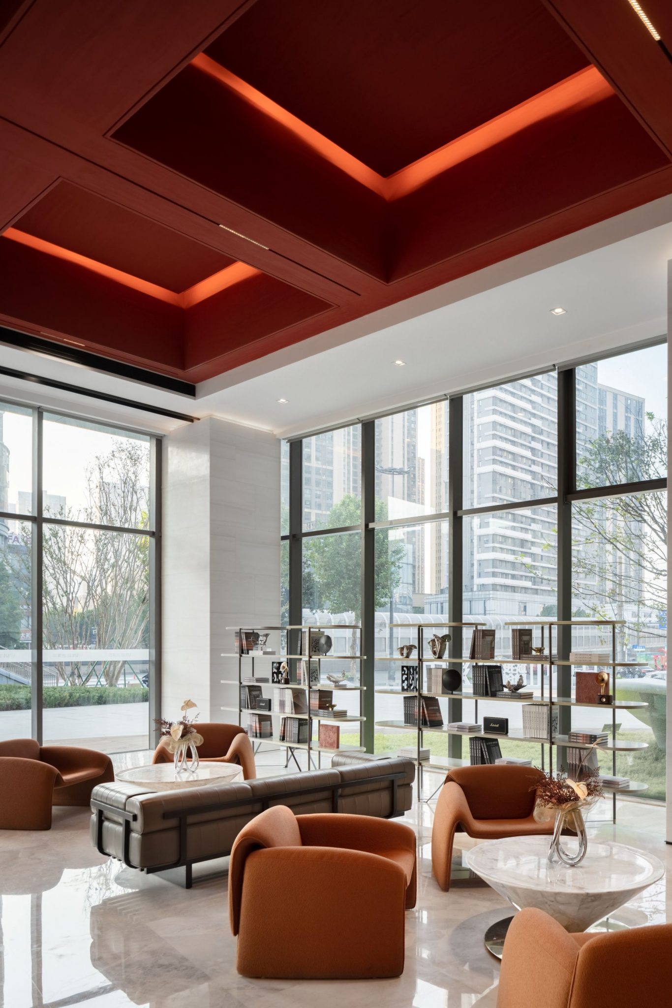 A modern lounge area with large windows, featuring a stylish ceiling and plush seating arrangements in warm tones.