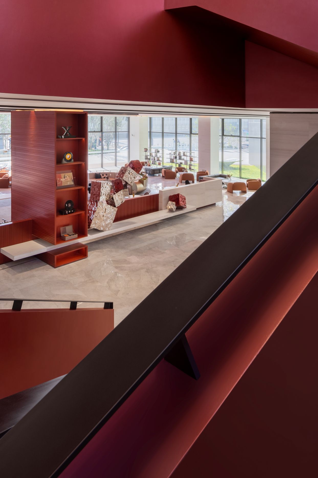 Interior view of a modern living space with red and neutral tones, featuring large windows, a sectional sofa, and decorative shelves.