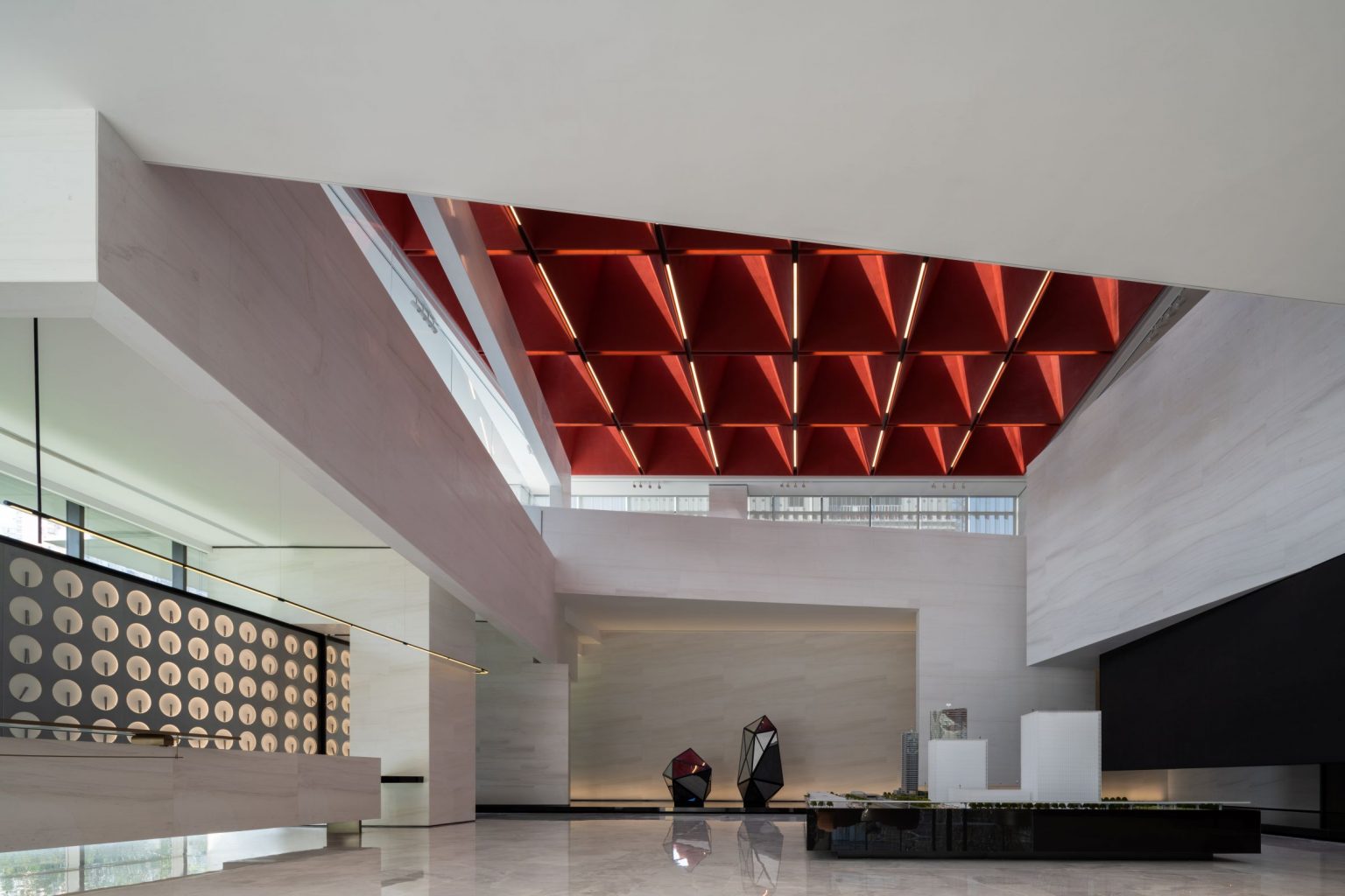 Modern interior of a lobby featuring geometric red ceiling panels, sleek furniture, and minimalist decor.