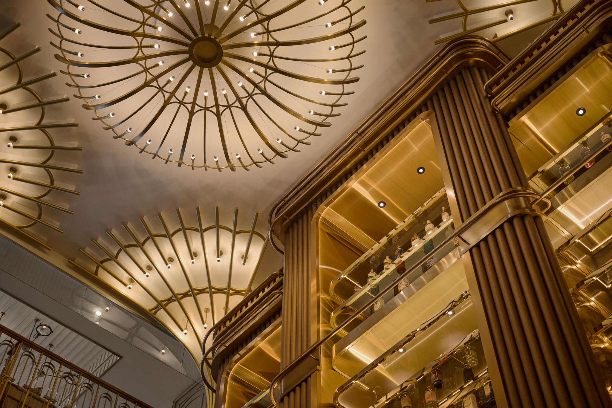 Ornate grand interior with golden balconies, towering fluted columns, and dramatic radial chandeliers glowing warmly overhead.