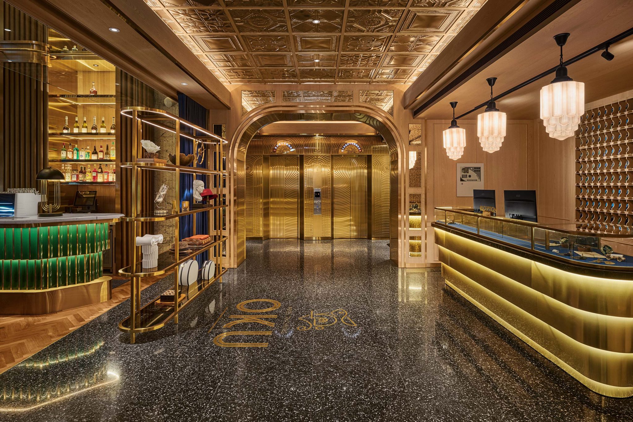 Luxurious hotel lobby with gold-trimmed elevator doors, marble floors, glowing reception desk, chandeliers, shelves, and warm elegant lighting.