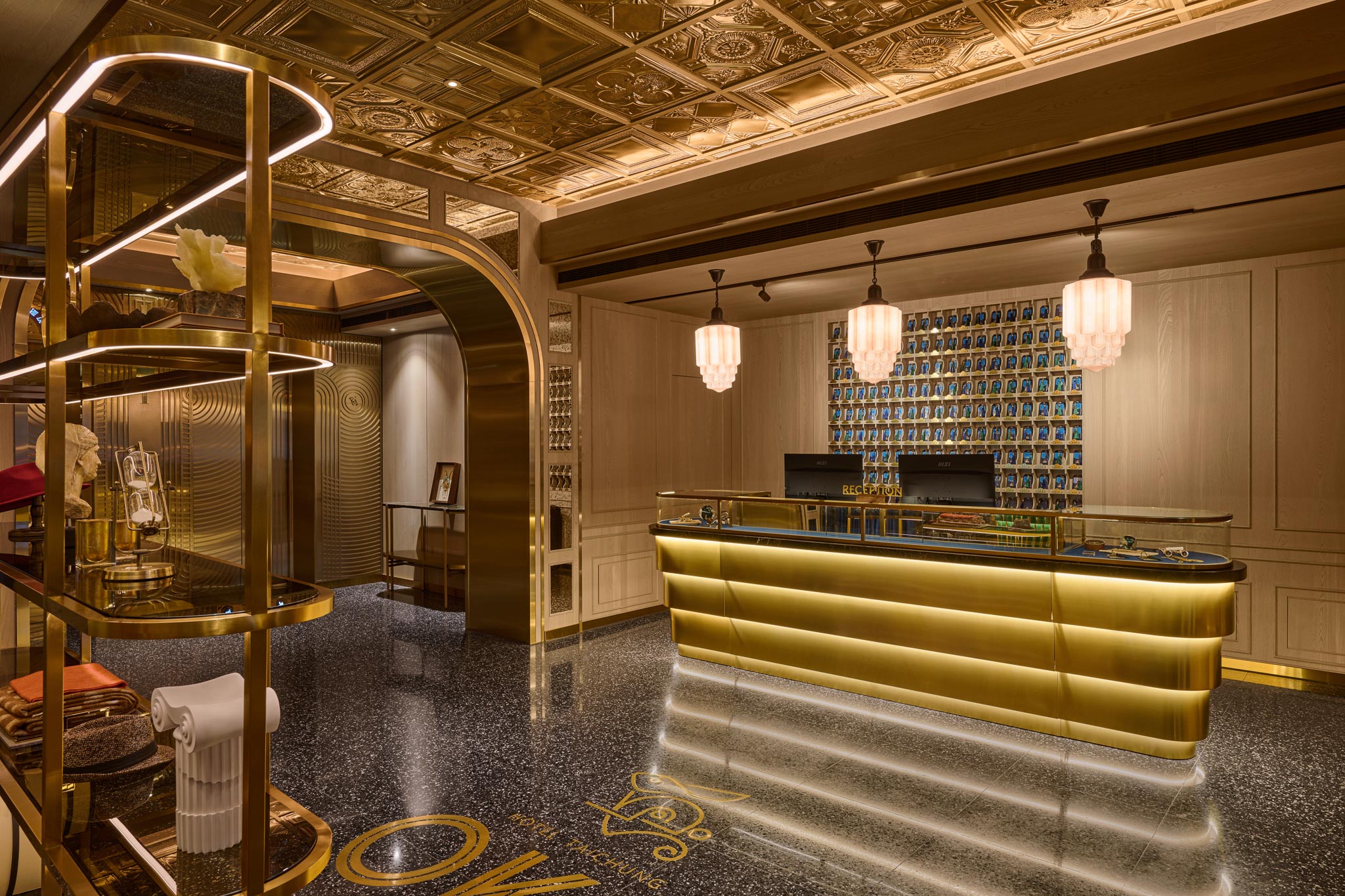 Luxurious hotel bar with a glowing gold counter, blue bottle display, pendant lights, ornate ceiling, and elegant art deco decor.