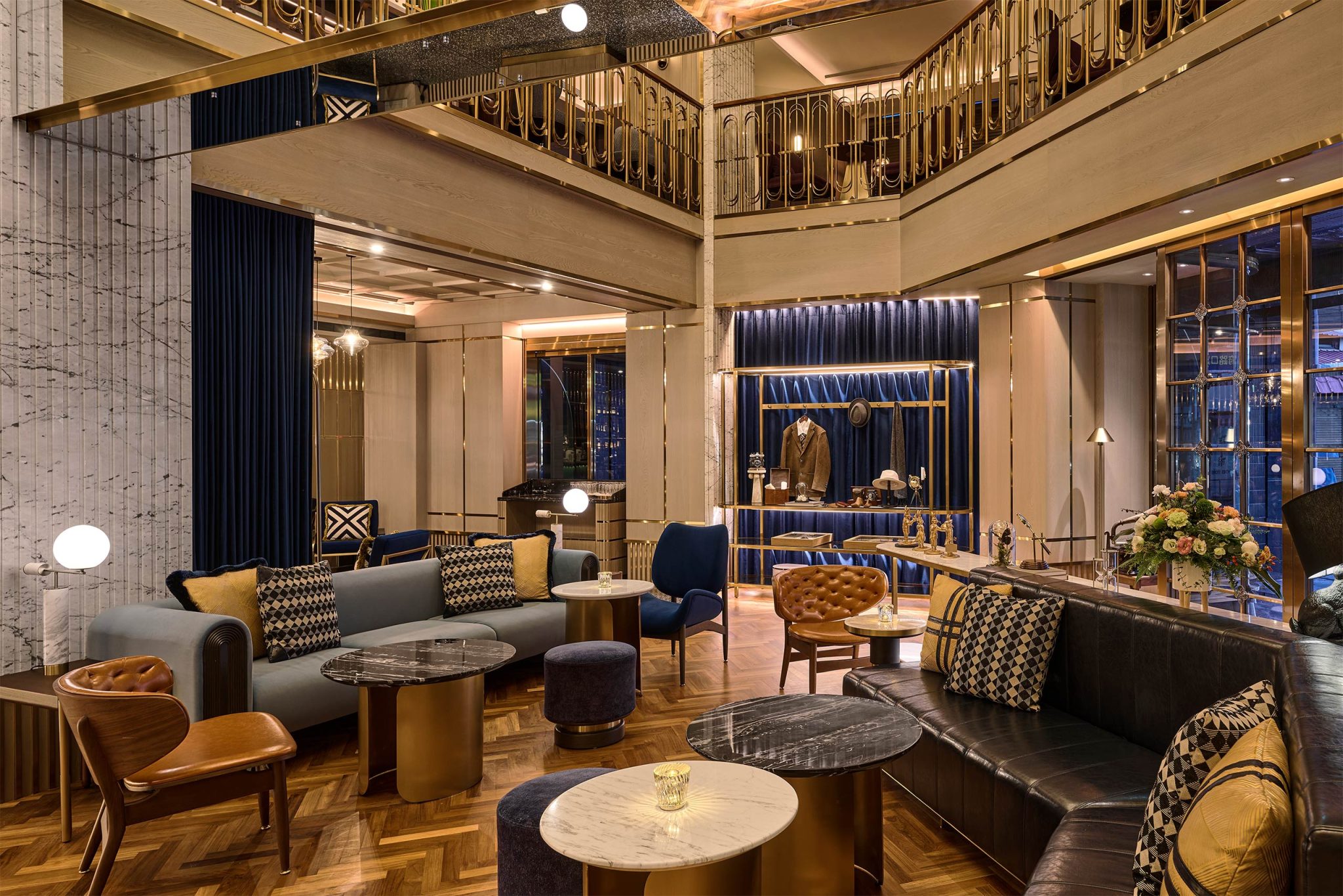Luxurious hotel lounge with velvet sofas, patterned cushions, marble tables, a bar, mezzanine balcony, and warm ambient lighting.