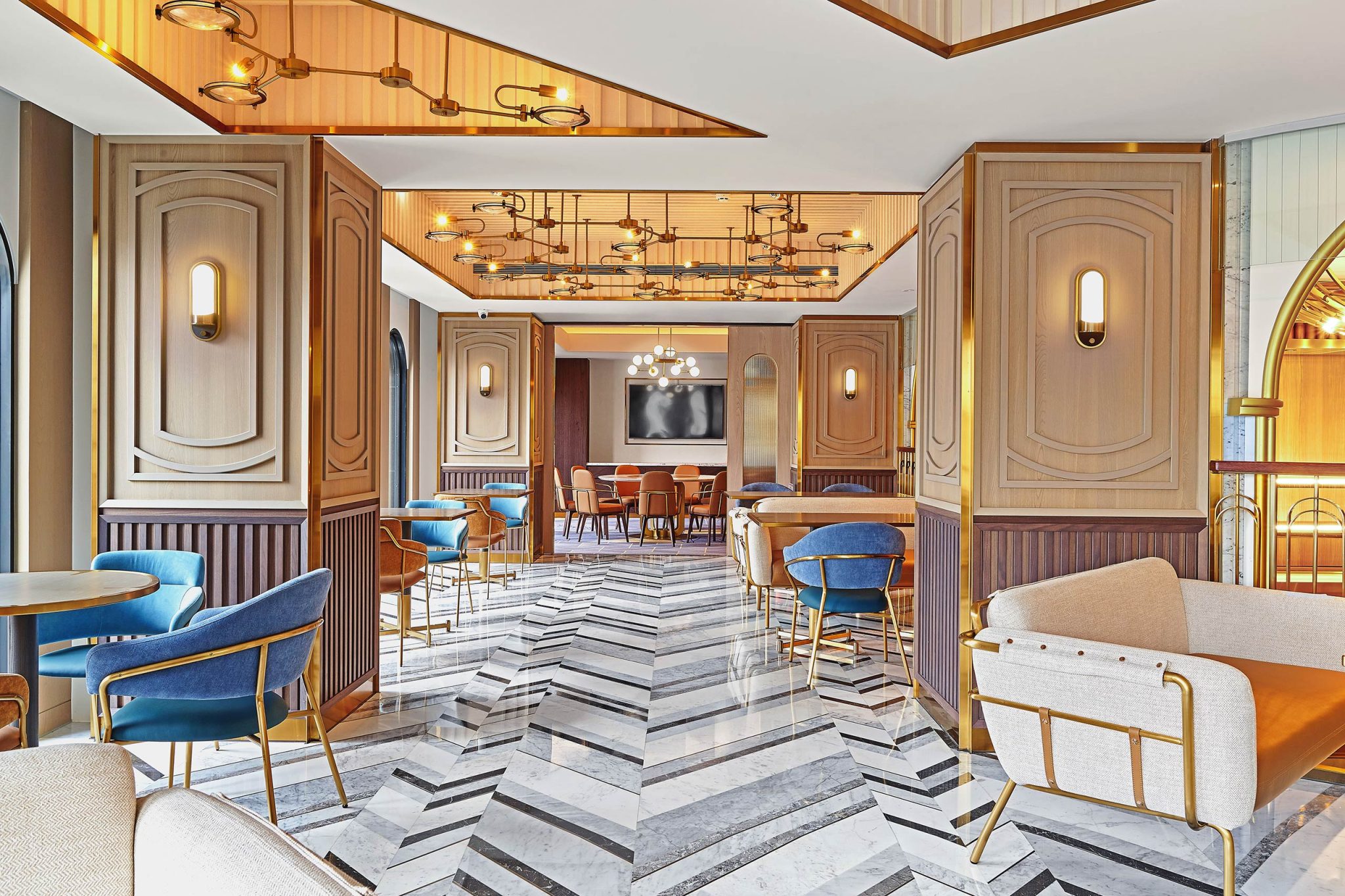 Elegant Art Deco hotel lounge with blue chairs, cream sofas, wood paneling, brass lights, and a dramatic gray-and-white marble floor.