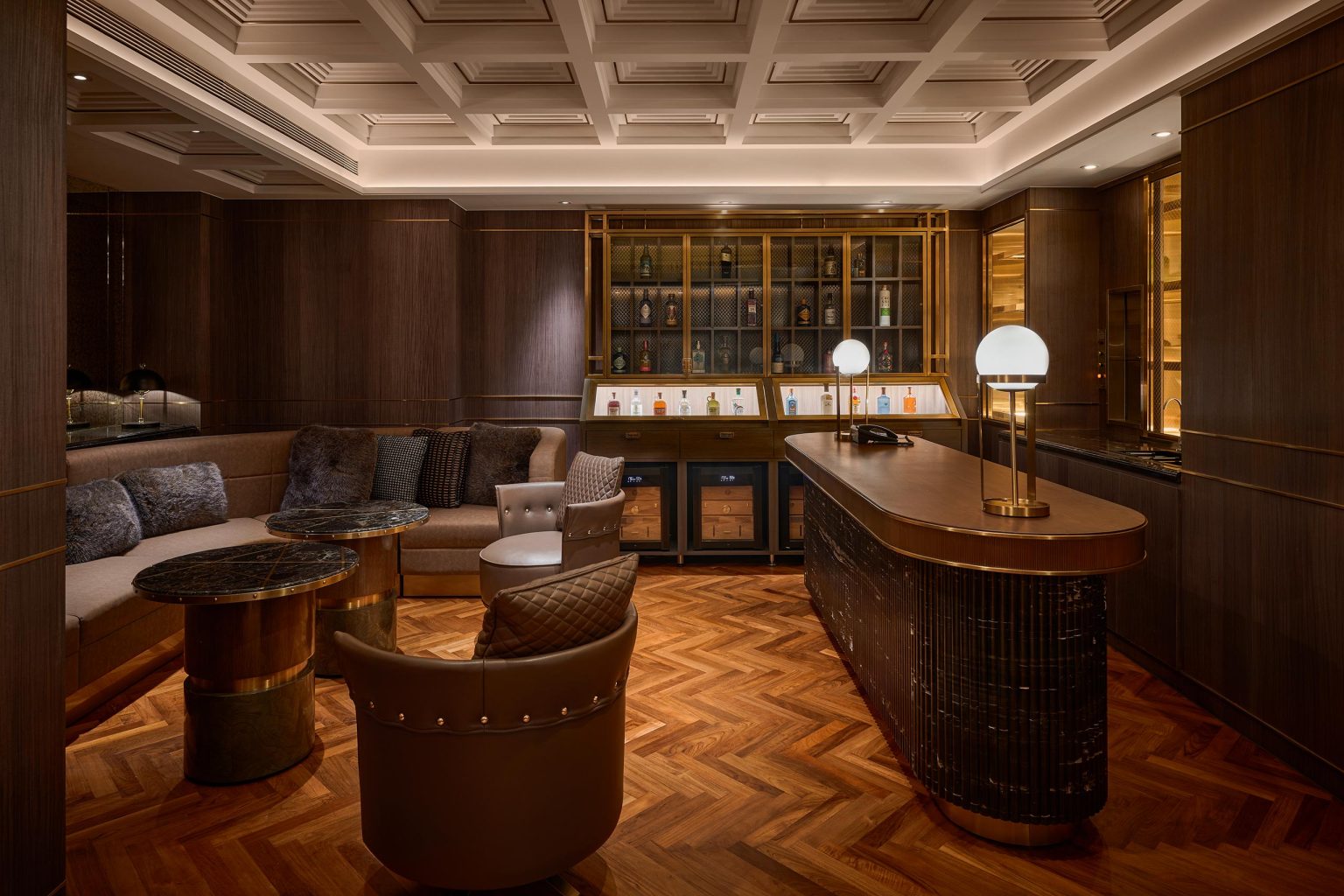 Luxurious dark-wood cigar lounge with brass accents, bar, lounge seating, marble counters, glass cabinets, warm lighting, and herringbone floors.